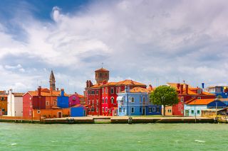 Colorful houses, church, boats and tower on the famous island Burano, view from the sea, Venice, Italy