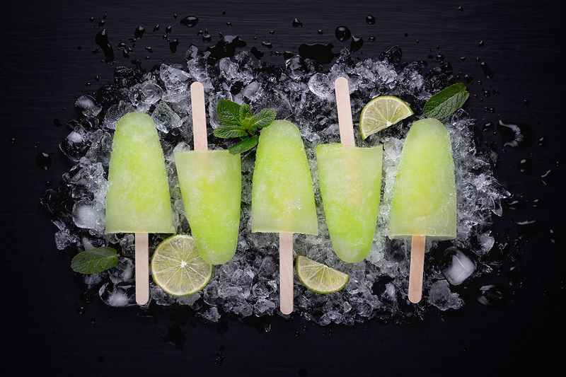 Homemade popsicles with lime juice and mint, mojito fruit ice on a black wooden table.