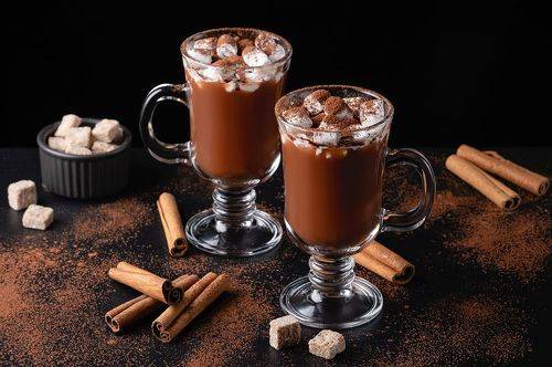 Two cups of hot chocolate, cocoa or warm drink with marshmallows on dark background.